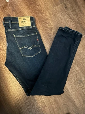 Mörkblå jeans från Replay W32 L34 - Snygga mörkblå jeans från Replay med klassisk femficksmodell och kontrastsömmar. Jeansen har en rak passform och detaljerad bakficka med broderi. Tillverkade i slitstark denim med en stilren look som passar till det mesta.