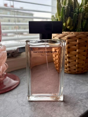 Musc Noir for Her parfym - Elegant parfymflaska i glas med svart rektangulärt lock från Narciso Rodriguez. Doften heter Musc Noir for Her och flaskan har en ljusrosa tonad vätska. Modern och stilren design som passar perfekt på sminkbordet. 100ml. Se bild hur mycket som använts 