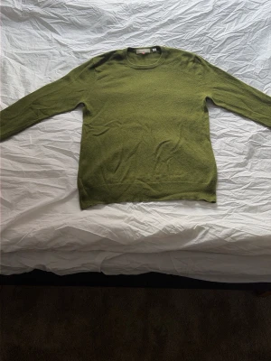 Olivgrön cashmeretröja från H&M - Snygg olivgrön stickad tröja från Uniqlo i mjuk cashmere. Tröjan har rund halsringning, långa ärmar och ribbade muddar vid ärmslut och nederkant. Den har ett litet hål vid bröstet. Perfekt för dig som gillar stilrena och bekväma plagg.