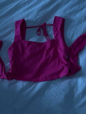 Rosa linnetopp med knytband - Trendig rosa linnetopp med breda axelband och knyt i ryggen. Toppen har en croppad passform och är perfekt för varma dagar. Tillverkad i mjukt bomullsmaterial som känns skönt mot huden. Enkel men snygg design som passar till mycket.