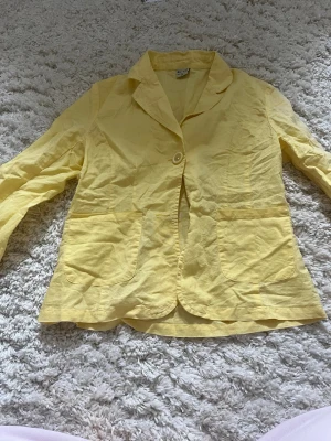 Gul kavaj - Snygg gul kavaj med enkelknäppning och två stora framfickor. Kavajen har klassisk krage och är tillverkad i ett lätt, skrynkligt tyg som ger en avslappnad look. Perfekt för dig som vill sticka ut med färg.