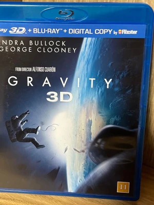 Gravity 3D Blu-ray + Digital Copy - Gravity 3D Blu-ray med digital kopia. Sci-fi film regisserad av Alfonso Cuarón med Sandra Bullock och George Clooney i huvudrollerna. Omslaget visar astronauter i rymden och jorden i bakgrunden. Inkluderar även 2D-version och nästan 3 timmar extramaterial.