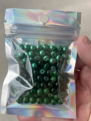 Gröna glaspärlor i holografisk påse - Säljer ett paket med glansiga, runda gröna pärlor i plast. Perfekta för att skapa egna smycken som armband, halsband eller örhängen. Pärlorna kommer i en snygg holografisk zip-påse som är enkel att återförsluta.
