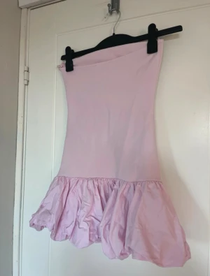 Ljusrosa volangklänning - Söt ljusrosa kort klänning med volang nedtill. Klänningen är axelbandslös och har en figurnära passform upptill med en fluffig kjoldel. Perfekt för dig som gillar en feminin och trendig stil. Nypris 300kr. Säljs inte längre. 