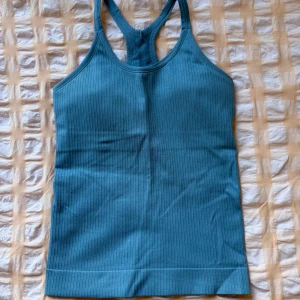 Blå ribbad linnetopp - Säljer en blå ribbad linnetopp från TRIDRI med brottarrygg. Toppen är ärmlös och har en tight passform. Materialet är mjukt och stretchigt för maximal komfort🦋