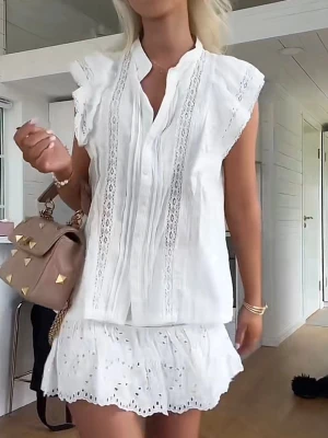 Vit blus med spetsdetaljer - Söt vit blus med broderade spetsdetaljer och volangkantade ärmhål. Blusen har en rak passform, v-ringad hals och knäppning framtill. Tillverkad i ett lätt och luftigt tyg, perfekt för sommardagar. Matcha med kjol eller jeans för en fräsch look.