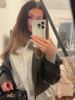 Svart skinnjacka i bikerstil - Snygg svart skinnjacka i klassisk bikerstil med dragkedja och breda slag. Jackan har en croppad passform och coola detaljer som ger en edgy look. Perfekt att slänga över en hoodie för en avslappnad streetstyle.