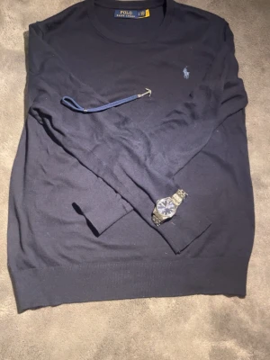 Mörkblå tröja från Polo Ralph Lauren - Klassisk mörkblå tröja från Polo Ralph Lauren med rund halsringning och diskret broderad logga på bröstet i grå färg . Tillverkad i mjukt material som passar perfekt till jeans eller chinos. Enkel och stilren design som funkar året runt.