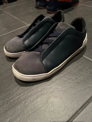 Mörkblå minimalistiska sneakers - Snygga sneakers i mörkblått med en clean och minimalistisk design. Ovandelen är i en mix av mocka och slätt läder, med mörk blå snören och vit sula. Perfekta för dig som gillar stilrena och moderna skor.