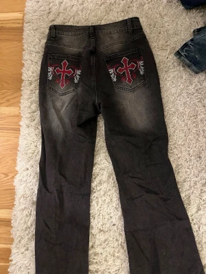 Svarta jeans med design på fickor -  svarta jeans med broderade bakfickor i rött och vitt. Materialet är denim med en tvättad look och detaljer som ger extra edge till outfiten. Aldrig använt