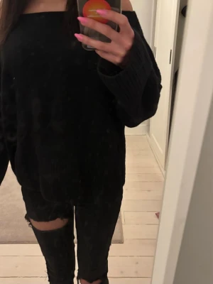 Svart off shoulder stickad tröja - Säljer en svart stickad tröja med off shoulder-design och långa, vida ärmar. Tröjan har en avslappnad passform och är perfekt för dig som gillar en trendig och bekväm stil. Materialet känns mjukt och stretchigt.