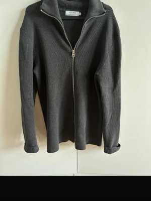 Mörkgrå ziptröja från Ljung - Stilren och mjuk stickad zip-tröja från Ljung i grått. Ett tidlöst plagg med dragkedja och hög krage. 	•	Storlek M 	•	Normal passform 	•	Mjuk, ribbstickad kvalitet 	•	Dragkedja framtill 	•	Hög krage 	•	Mycket fint skick  Ger en clean, minimalistisk look och passar lika bra till jeans som chinos eller över skjorta.  Nypris: 1 200 kr