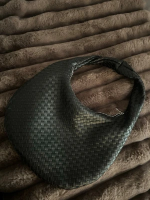 Svart flätad axelväska - Säljer en svart handväska med flätad design och rundad form. Väskan har en kort axelrem och stängs med dragkedja. Köpt på ginatricot för 500🩷