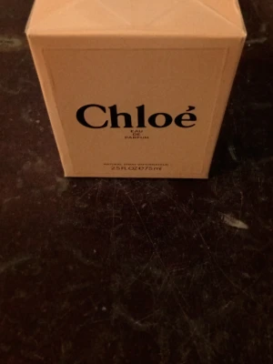 Chloé Eau de Parfum 75 ml - Chloé Eau de Parfum i en elegant beige kartong med svart text. Flaskan innehåller 75 ml och doften är känd för sin fräscha, blommiga och feminina karaktär. Förpackningen har en stilren och lyxig känsla, perfekt för dig som gillar klassiska parfymer.