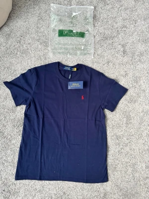 Marinblå t-shirt från Polo Ralph Lauren - Snygg marinblå t-shirt från Polo Ralph Lauren med klassisk röd logga broderad på bröstet. T-shirten har rund halsringning och korta ärmar. Tillverkad i mjuk bomull för en bekväm känsla. Perfekt till jeans eller shorts.