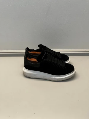 Svarta Alexander McQueen sneakers - Stilrena svarta sneakers från Alexander McQueen med tjock vit sula och svarta skosnören. Orginal storlek 41. Skorna är i mycket bra skick. Ovandelen är i mocka och läder, och modellen har en klassisk låg profil som passar till det mesta. Diskret logga på plösen och hälen. Priset ej hugget i sten. Hör av er vid frågor eller funderingar! 