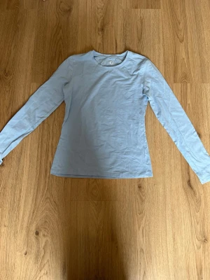 Ljusblå långärmad topp - En enkel och stilren ljusblå långärmad topp med rund halsringning. Toppen har en slim passform och är tillverkad i mjuk bomull, perfekt att matcha med jeans eller kjol för en clean look.