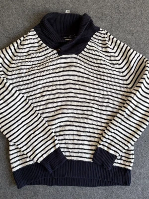 Randig stickad tröja från Nautica - Snygg stickad tröja från Nautica i marinblått och vitt med horisontella ränder. Tröjan har en hög, ribbstickad krage och muddar vid ärmslut och nederkant. Perfekt för dig som gillar klassisk, nautisk stil och vill ha något både bekvämt och trendigt.