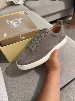 Gråa sneakers från Louboutin - Snygga gråa sneakers från Louboutin i mocka med vita sulor och gråa skosnören. Klassisk låg modell med stilren design och diskreta detaljer. Perfekta för dig som gillar exklusiva och trendiga skor.