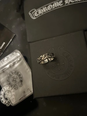😎 HELT NY ring Chrome Hearts med mönster - Säljer en snygg silverring från Chrome Hearts med detaljerat, svartoxiderat mönster runt hela ringen. Ringen har en klassisk, bred form och är tillverkad i äkta silver. Perfekt för dig som gillar streetwear och exklusiva accessoarer. SKRIV PÅ MED FRÅGOR, FINNS FLERA MODELLER TYP 12 st? Checka sidan. kan göra deals vid KÖP AV FLERA 😎😎‼️