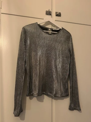 Silvrig topp - Silvrig topp i tunt tyg och med öppen rygg. I storlek M från NAKD. Endast använd några få gånger.