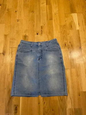 Blå jeanskjol Closed  med slits stl 42 - Snygg blå jeanskjol i klassisk modell med fickor fram och bak, bälteshällor och knappstängning. Kjolen har en liten slits bak för extra rörelsefrihet. Perfekt till sneakers eller boots för en avslappnad look.