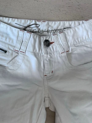 Lågmidjade vita jeans  - Snygga vita jeans från Esprit med coola detaljer som kontrastsömmar i rött och dragkedjor på bakfickorna. Skriv med frågor!💕