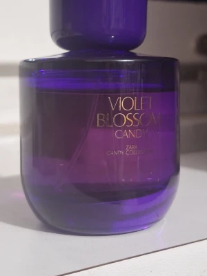 Zara Violet Blossom Candy parfym + Rituals  - En parfym från Zara i serien Candy Collection, doften Violet Blossom Candy. Flaskan är rund och lila med guldfärgad text. Innehåller 90 ml Eau de Parfum och är tillverkad i Spanien. Perfekt för dig som gillar söta och blommiga dofter.