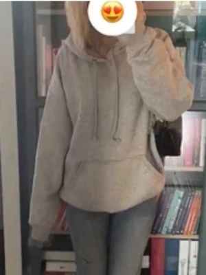 Grå hoodie med huva och ficka - En klassisk grå hoodie med stor huva och dragsnören. Hoodien har en rymlig magficka och ribbade muddar vid ärmslut och nederkant. Perfekt för en avslappnad och chill look. Materialet är mjukt och bekvämt, troligen bomullsblandning.