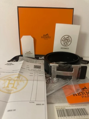  svart bälte  med H-spänne - Snyggt svart bälte med ikoniskt H-spänne i silverfärgad metall. Skärpet är tillverkat i exklusivt skinn och levereras med originalförpackning och tillbehör. Perfekt accessoar för att lyfta din outfit.