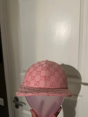 Rosa GG keps med  - Säljer en rosa keps från GUCCl med det klassiska GG-monogrammet över hela kepsen. Kepsen har böjd skärm och justerbart band bak. Materialet är canvas med insida i ljus textil. Perfekt för dig som vill ha en statement-accessoar.