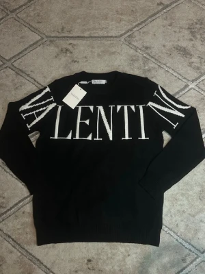 Svart stickad tröja från Valentino - Svart stickad tröja från Valentino med stor vit logotyp över bröstet och ärmarna. Tröjan har rund halsringning och långa ärmar. Perfekt för dig som gillar statement-plagg och exklusiva märken.