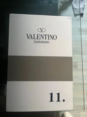 Valentino Garavani vita sneakers - Snygga vita sneakers från Valentino Garavani med en bred svart rem över sidan. Skorna har klassisk låg profil, rund tå och är tillverkade i läder. Perfekta inför sommaren och för dig som vill ha en stilren look. Passar för dig som har 43 i storlek också. 