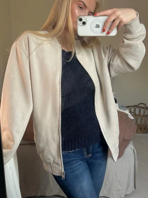 Beige bomberjacka i mockaimitation - Fantastiskt skick 🥰Jackan har en mjuk yta som påminner om mocka och ribbade muddar vid ärmslut och nederkant. 