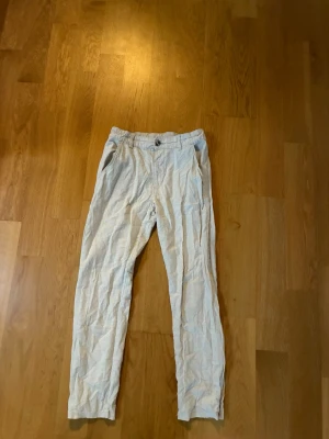 Beiga linnebyxor med resår - Snygga beiga linnebyxor med resår i midjan och raka ben. Byxorna har sidfickor och stängs med knapp och dragkedja framtill. Perfekta för en avslappnad och stilren look. Perfekt när sommaren väntar runt hörnet. 