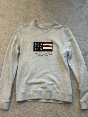 Grå sweatshirt från Lexington - Storlek M, sweatshirt från Lexington med broderad logga och flaggdetalj på bröstet. Perfekt för en avslappnad och snygg look. 