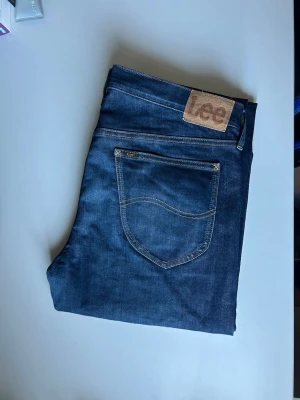 Mörkblå jeans från Lee - Snygga mörkblå jeans från Lee med klassisk femficksdesign och kontrastsömmar. Jeansen har en rak passform och är tillverkade i slitstarkt denimtyg. Perfekta för dig som gillar en tidlös och enkel stil.