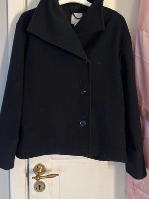 Marinblå kappa - Stilren marinblå kappa med snygg asymmetrisk knäppning och bred krage. Kappan har tre knappar framtill och raka ärmar. Perfekt för dig som gillar minimalistisk och modern stil.