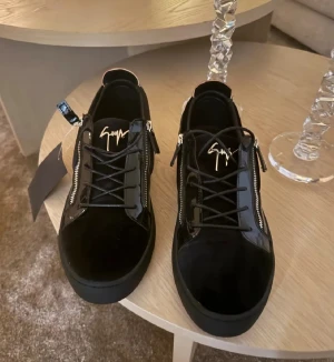 Svarta sneakers från Giuseppe Zanotti - Snygga svarta sneakers från Giuseppe Zanotti med lackdetaljer, dragkedjor på sidorna och signaturlogga på plösen. Skorna har en chunky sula och är tillverkade i en mix av mocka och skinn. Perfekta för dig som vill ha en exklusiv och trendig look.  jag fick de som present men tyvärr passa de inte och de var inte min styl, jag bruka ha baggy style. skorna är använt ett par gånger men tagg e fortffarande på. 