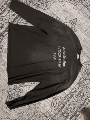 Svart långärmad tröja Acne Studios - Cool svart långärmad tröja från Acne Studios med tryck i vitt framtill där det står 'Acne Studios STOCKHOLM 1996'. Tröjan har rund halsringning. Köpt från plick, lite för stor för mig