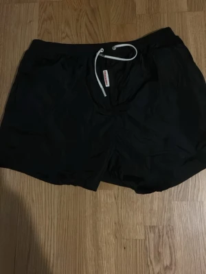 Svarta badbyxor från Dsquared2 - Säljer ett par svarta badbyxor från Dsquared2 med vit dragsko i midjan. Tillverkade i 100% polyamid för en lätt och snabbtorkande känsla. Klassisk modell med elastisk midja och diskret logga på snöret. Perfekta för stranden eller poolen.
