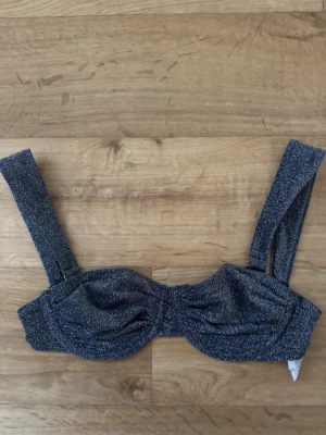Glittrig bandeau-bh - Snygg bandeau-bh  med glittrigt tyg och breda axelband. Bh:n har lätt rynkade kupor och en stilren design utan synliga detaljer. Perfekt för dig som vill ha något trendigt och bekvämt med lite extra glans.