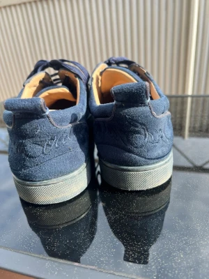 Christian Louboutin marinblå - Snygga mörkblå Christian Louboutinskor med matchande skosnören, diskret broderad logga på hälen och röd undersida. 