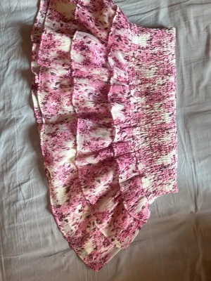 Rosa blommig volangkjol - Supersöt kort kjol med rosa och vita blommor och flera volanger. Den är egentligen högmijat men det går att vika ner den till lågmidjat kan skicka bild hur det ser ut!