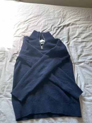 Mörkblå stickad tröja med halvzip - Mörkblå stickad tröja gjord i merinoull. Den är lite sliten men inga hål eller något sånt på tröjan. Tröjan är köpt för 899 kr.