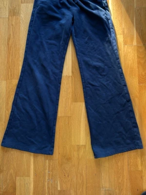 Mörkblå mjukisbyxor från Gina Tricot - Mörkblå mjukisbyxor från Gina Tricot med utsvängda ben och resår i midjan. Tillverkade i mjukt och bekvämt material som passar perfekt för en avslappnad stil. Snygg och enkel design som är lätt att matcha med olika toppar.