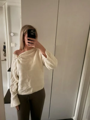 Off shoulder stickad tröja i creme - Trendig cremefärgad stickad tröja med off shoulder-design och lös passform. Tröjan har långa ärmar och en snygg detalj vid axeln. Perfekt för dig som gillar en avslappnad men stilren look.