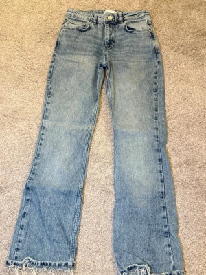Ljusblå raka jeans med fransad kant - Säljer ett par ljusblå jeans med raka ben och fransad kant nertill. Klassisk femficksmodell och hög midja. Jeansen har en avslappnad passform och är tillverkade i denim. Perfekta för en cool och avslappnad stil.