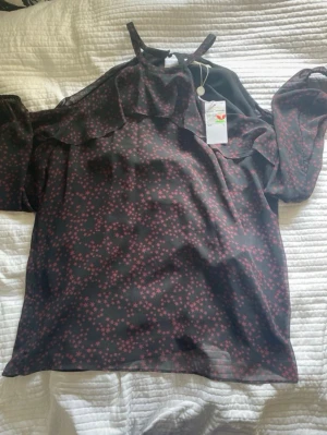 Michael kors offshoulder-blus äkta - Helt ny orginal pris 1699. Pris kan diskuteras vid snabb affär. Den känns som en M. Snygg svart blus med små rosa blommor och offshoulder-modell från Michael kors. Blusen har volangdetaljer upptill och tunna axelband. Lätt och luftig i transparent material, perfekt för en trendig look. Rök, vap och husdjursfritt hem. 