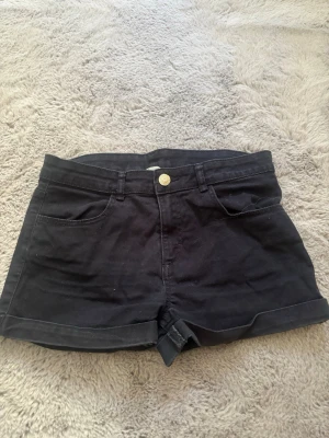 Svarta shorts - Snygga svarta shorts med medel midja och uppvikta benslut. Klassisk femficksmodell med knapp och dragkedja framtill. Perfekta till sommaren och lätta att matcha med olika stilar.